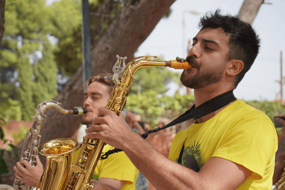 Dos saxofonistas de Baloo's Band con camiseta amarilla bajo un árbol